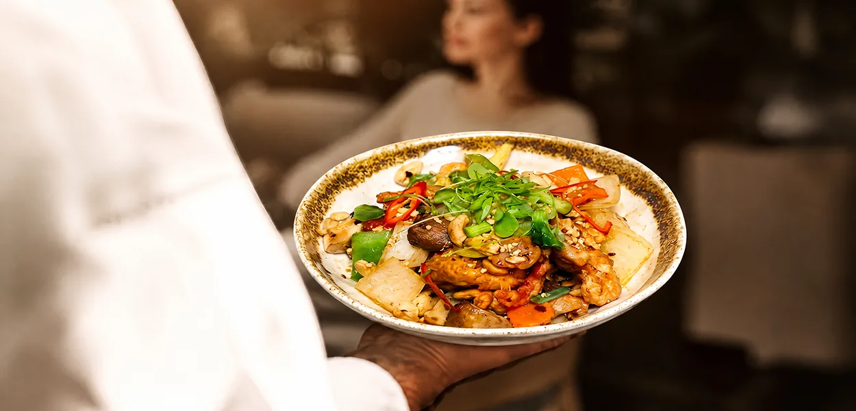 Server carrying a plate of chicken and cashew nut stir-fry with peppers and microgreens at Nara Thai
