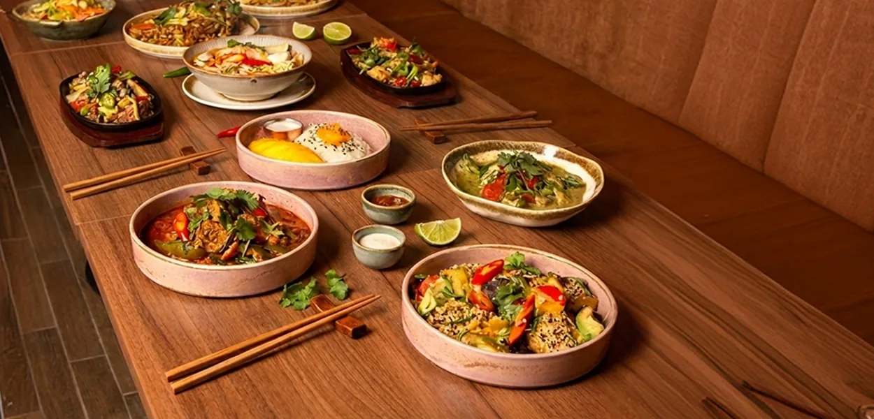 Thai dishes in ceramic bowls and on sizzling plates with chopsticks on a wooden table at Nara Thai