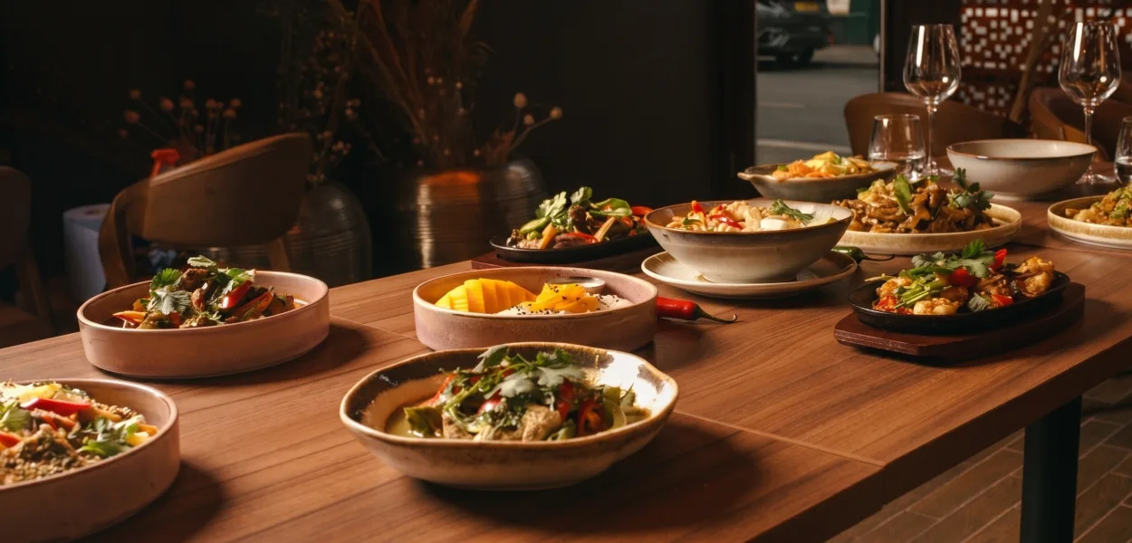 Thai dishes in ceramic bowls and on sizzling plates on a wooden table beside the window at Nara Thai