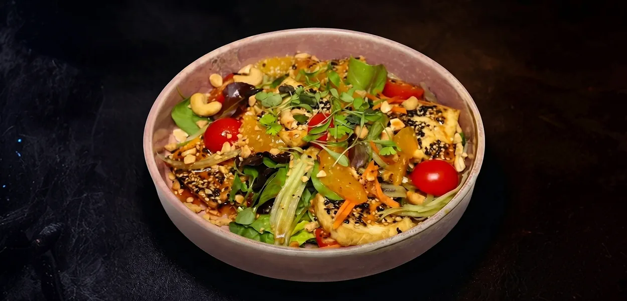 Tofu salad with sesame seeds, cashew nuts, cherry tomatoes and mixed leaves in a ceramic bowl at Nara Thai