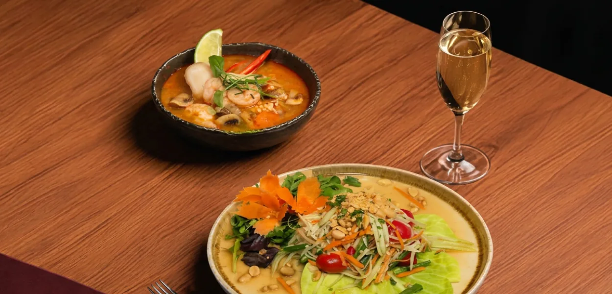 Tom yum soup with prawns and a papaya salad with peanuts beside a glass of white wine at Nara Thai