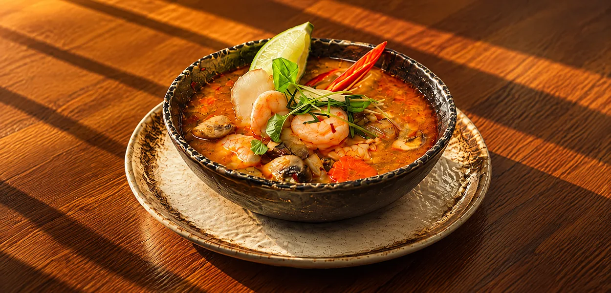Tom yum soup with prawns, mushrooms, lime and red chilli in a dark speckled bowl at Nara Thai